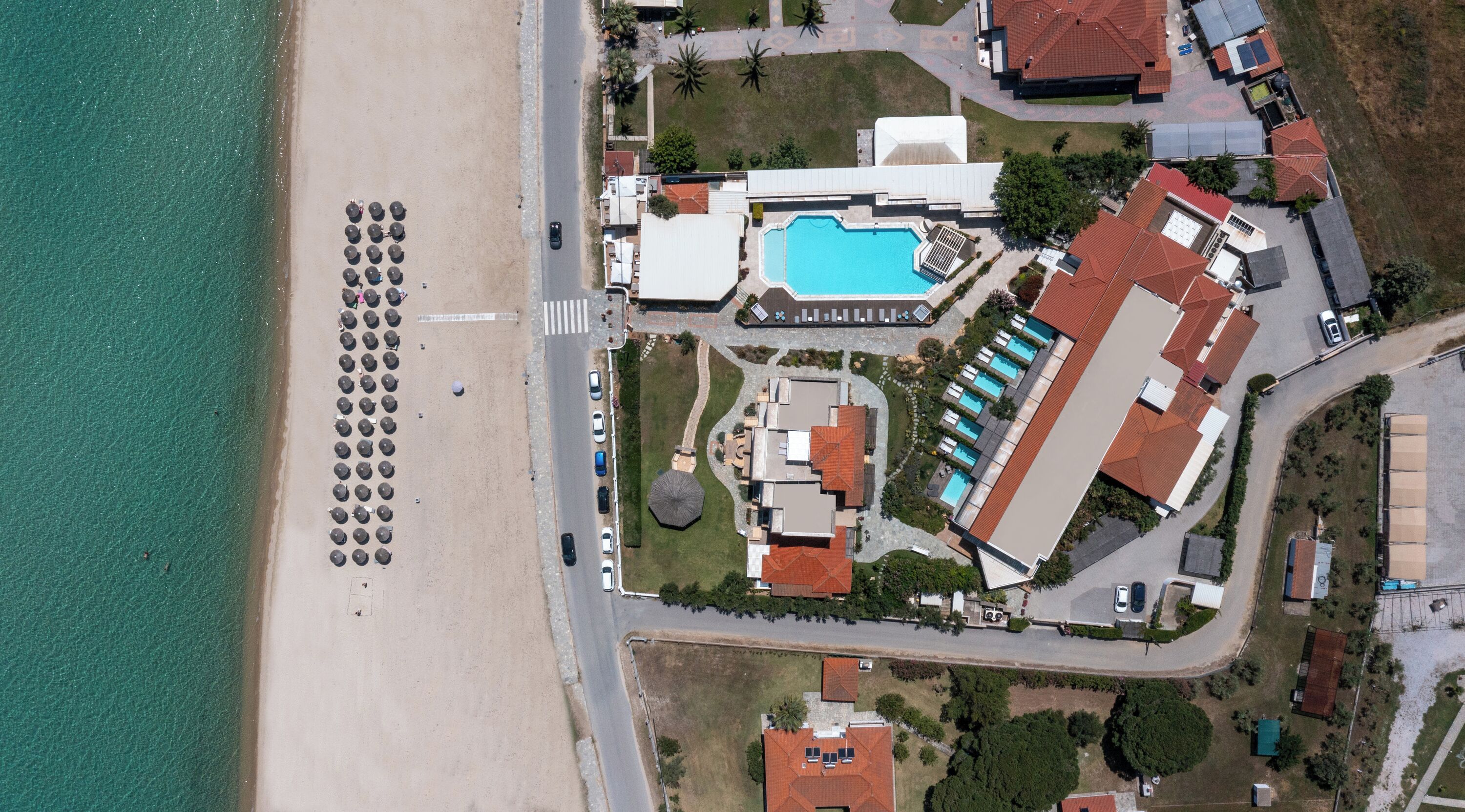 An aerial view of a coastal resort with a beach, a swimming pool, and multiple buildings.