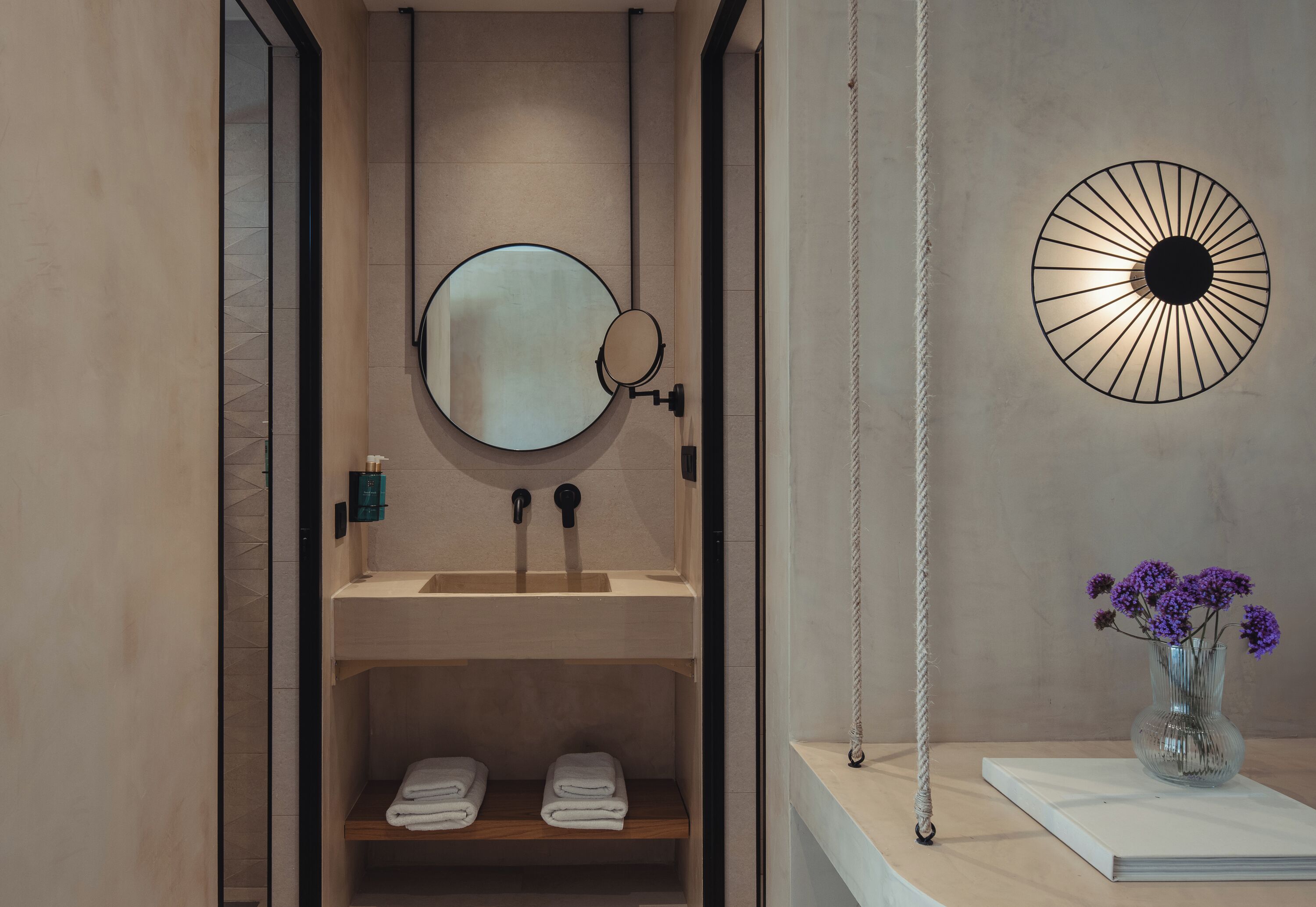 Un baño moderno con un espejo redondo, un lavamanos y un estante con toallas.