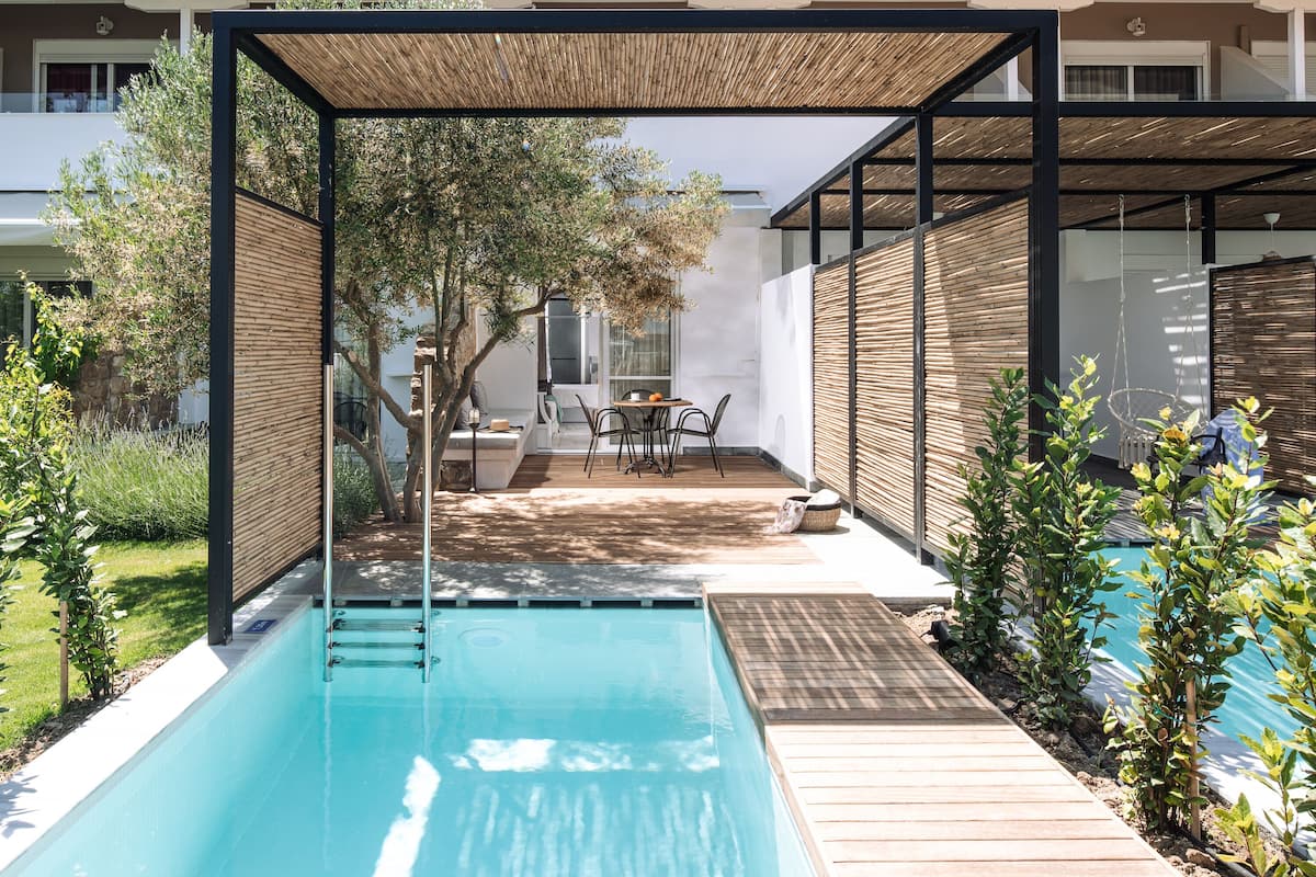 Un área de piscina moderna al aire libre con un deck de madera, una zona de estar cubierta y vistas al jardín circundante.