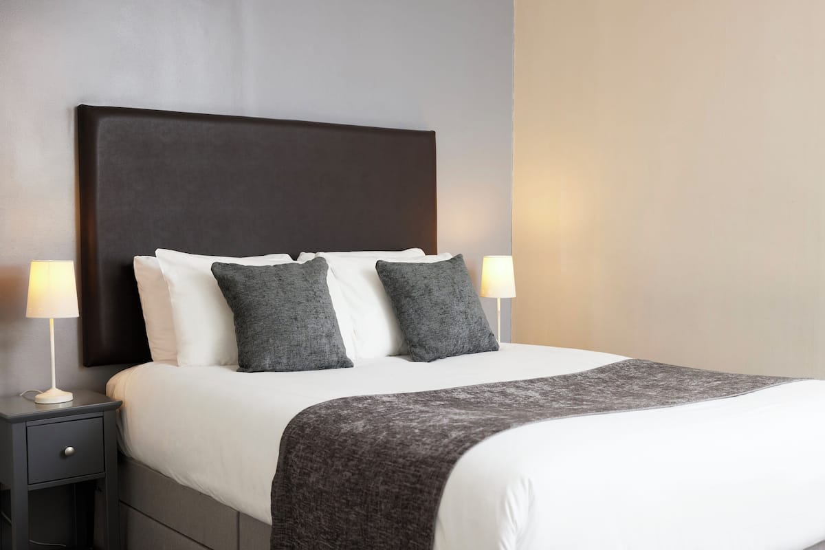 A neatly made bed with a dark headboard, two bedside lamps, and a gray throw blanket.
