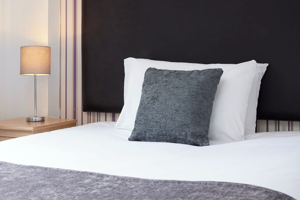 A neatly made bed with white and grey bedding, a dark headboard, and a striped wall with a framed picture.