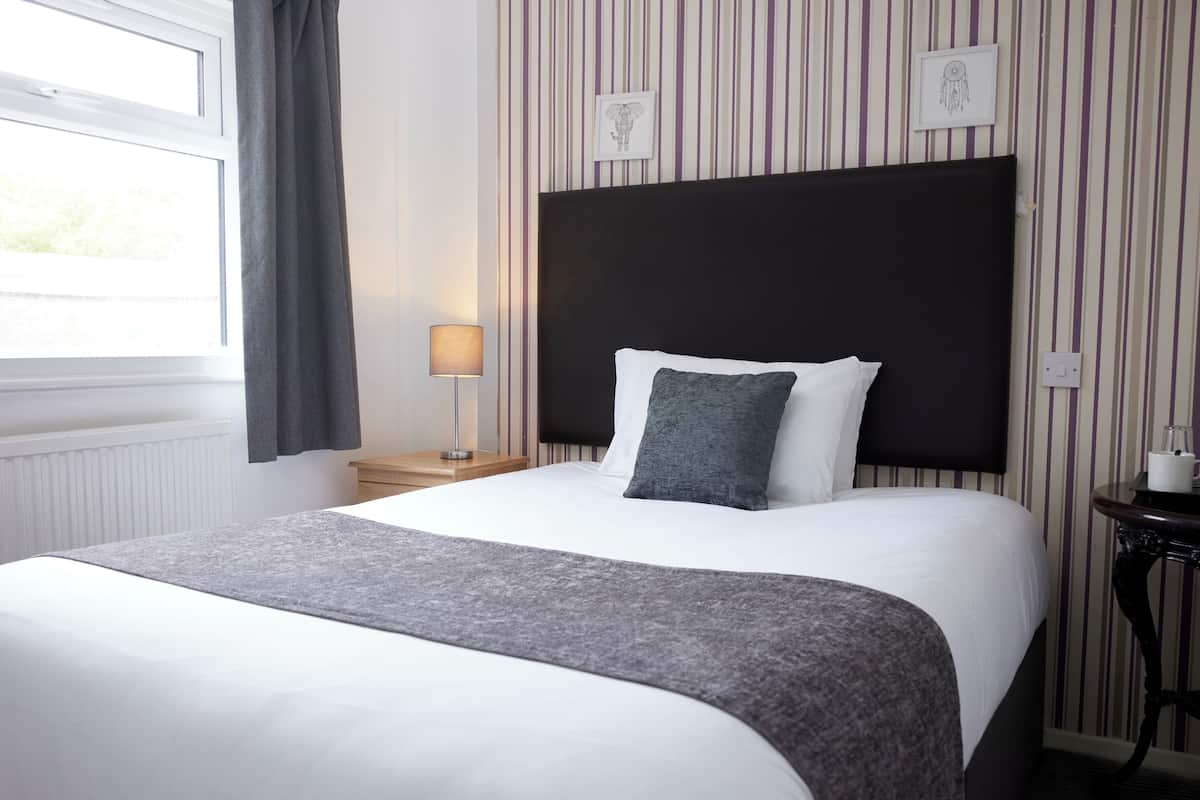 A neatly made bed with a grey blanket, a black headboard, and a bedside table with a lamp.