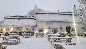 A snow-covered building with multiple windows and a courtyard with picnic tables. - Old Ferry Boat St Ives by Greene King Inns (St Ives)