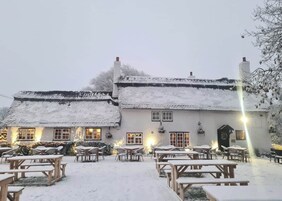 Um edifício coberto de neve, com várias janelas e um pátio com mesas de piquenique.