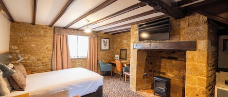 A cozy room with a bed, a desk, a fireplace, and a television.