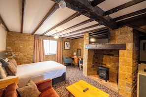 A cozy room with a bed, a desk, a fireplace, and a television.