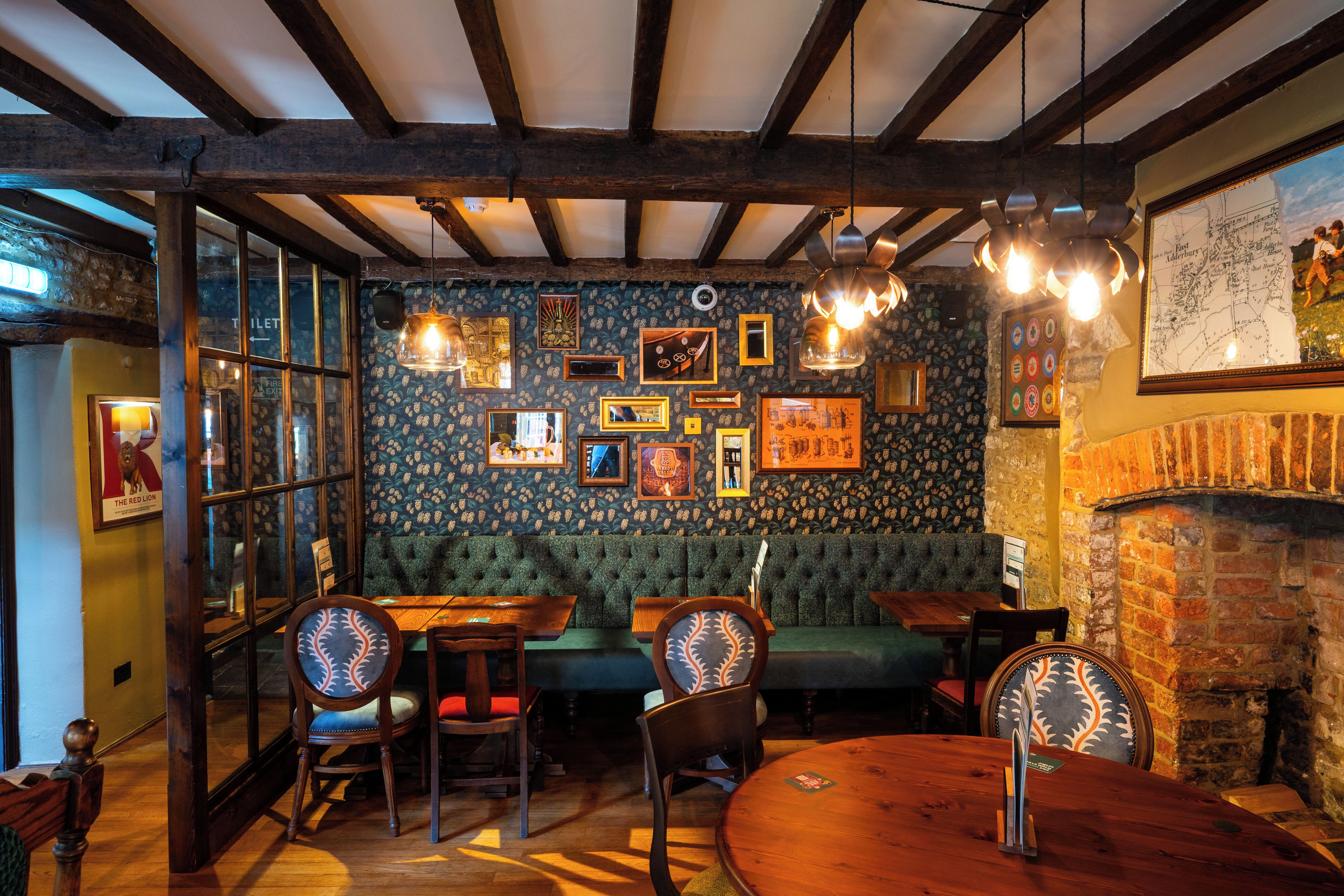 A cozy pub interior with exposed wooden beams, a green upholstered bench, and a brick wall.