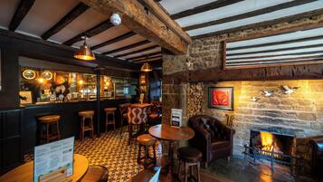 A bar area with wooden beams, a stone wall, a fireplace, and a checkered floor.