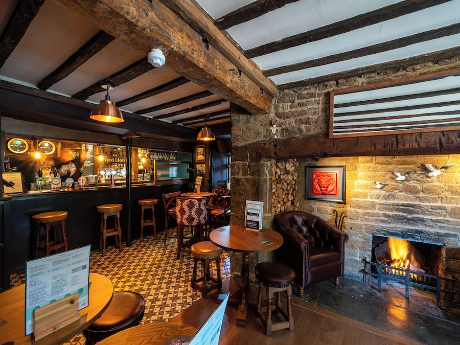 A bar area with wooden beams, a stone wall, a fireplace, and a checkered floor.
