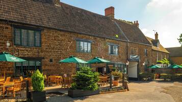 A traditional stone building with a sign reading 'THE RED LION' and outdoor seating with umbrellas.
