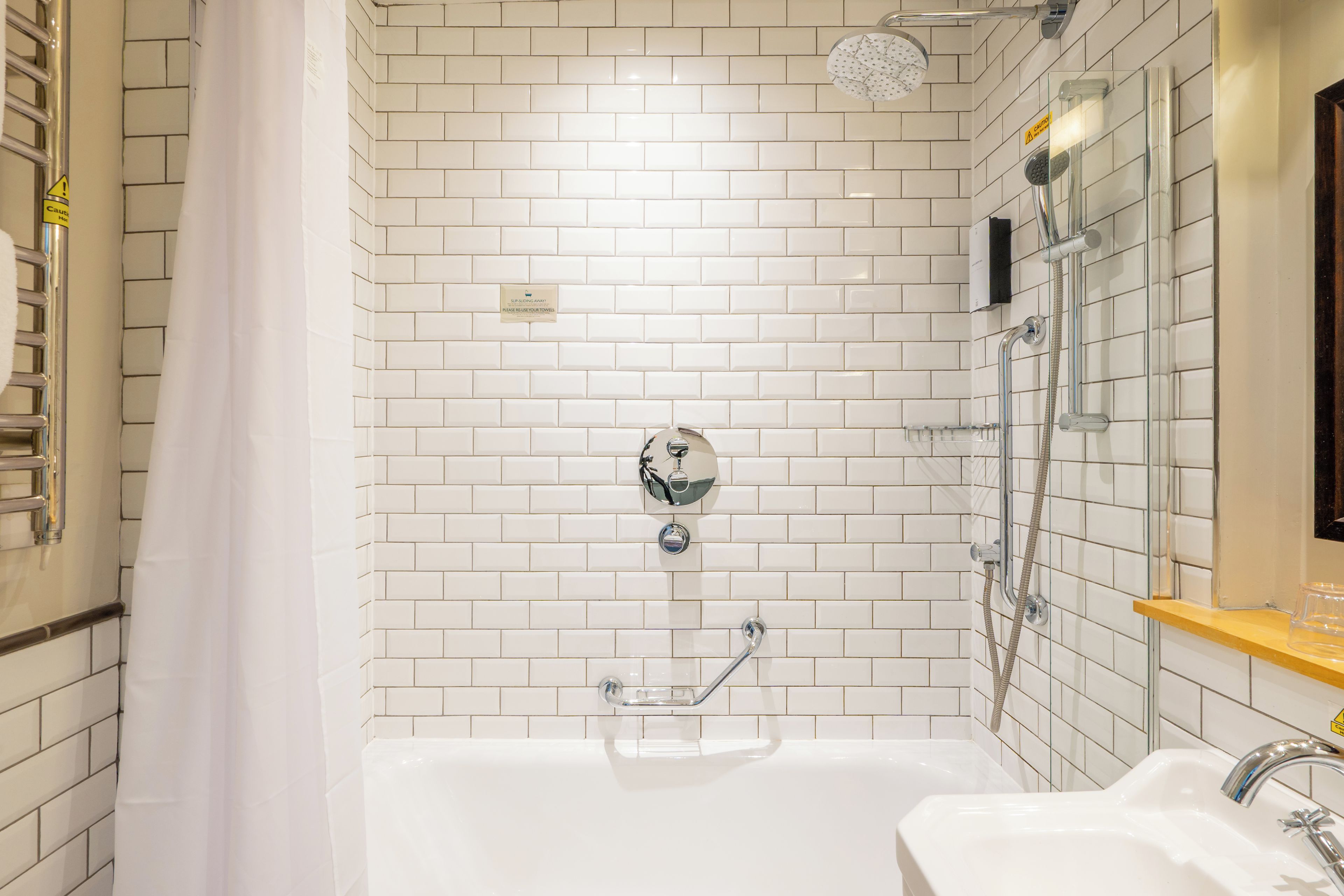 Une salle de bain avec des murs carrelés de carrelage blanc, une baignoire, un espace douche et un lavabo.