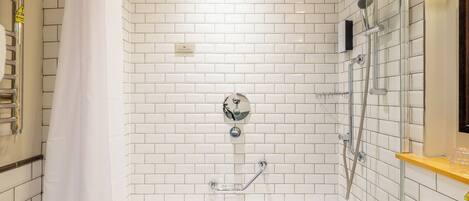 Une salle de bain avec des murs carrelés de carrelage blanc, une baignoire, un espace douche et un lavabo.