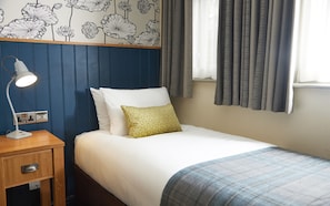 A neatly made bed with white and blue bedding, a bedside lamp, and a wall with a floral pattern. - Red Lion Hotel Adderbury by Greene King Inns (Banbury)