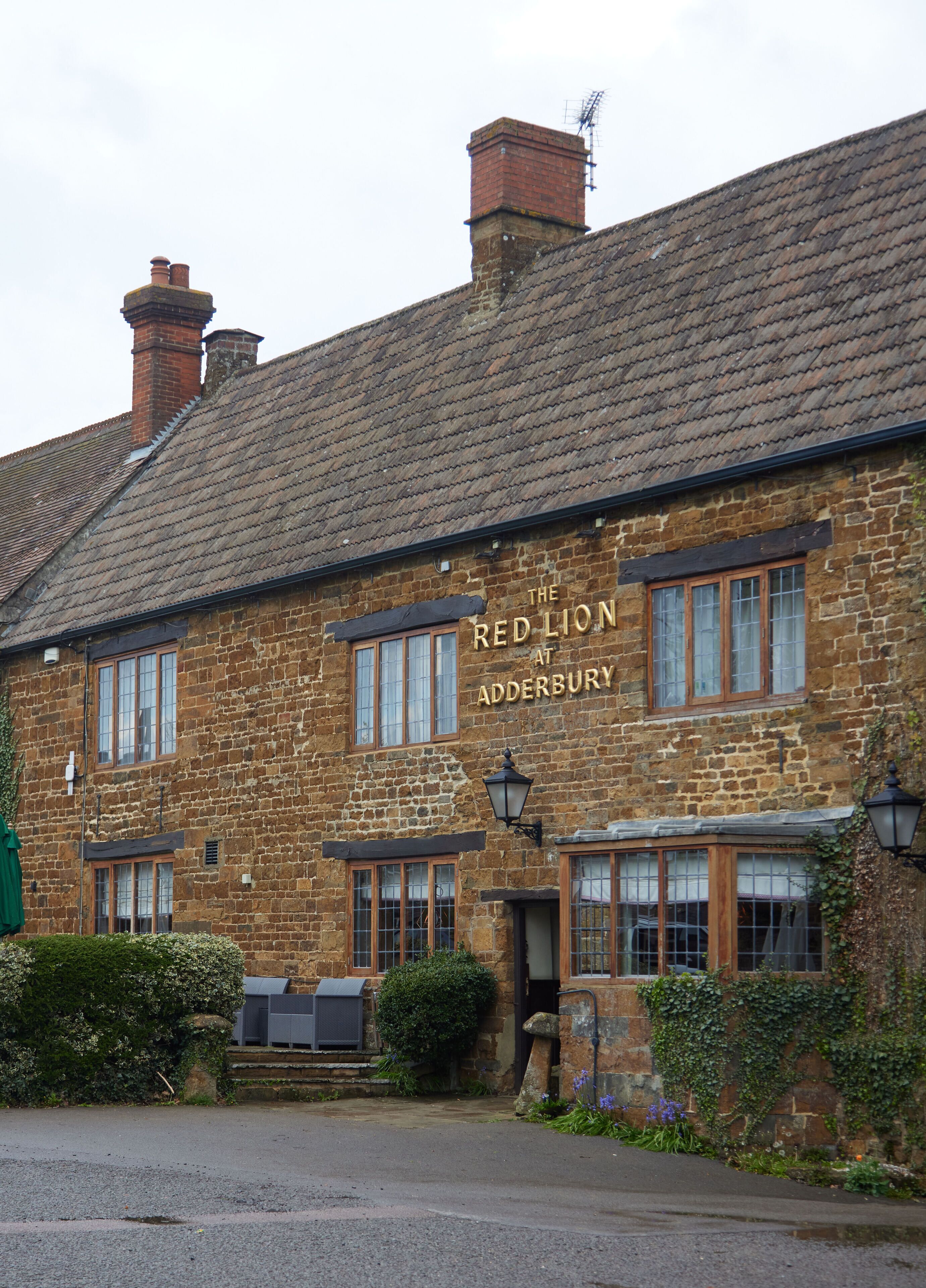 Un edificio de piedra con un letrero que dice "The Red Lion at Adderbury".