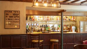Uma área de bar com móveis de madeira, diversos tipos de garrafas e um aviso na parede.