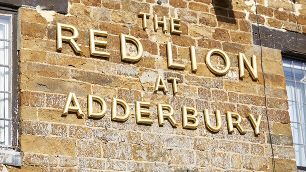 Paredes de tijolo com o texto "THE RED LION AT ADDERBURY" em letras douradas.