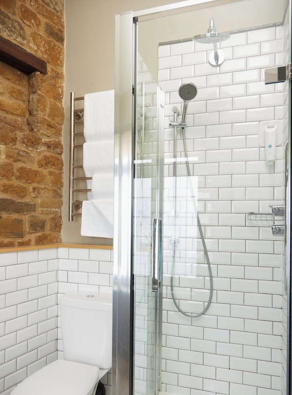 A glass-enclosed shower with a handheld showerhead and a wall-mounted faucet.