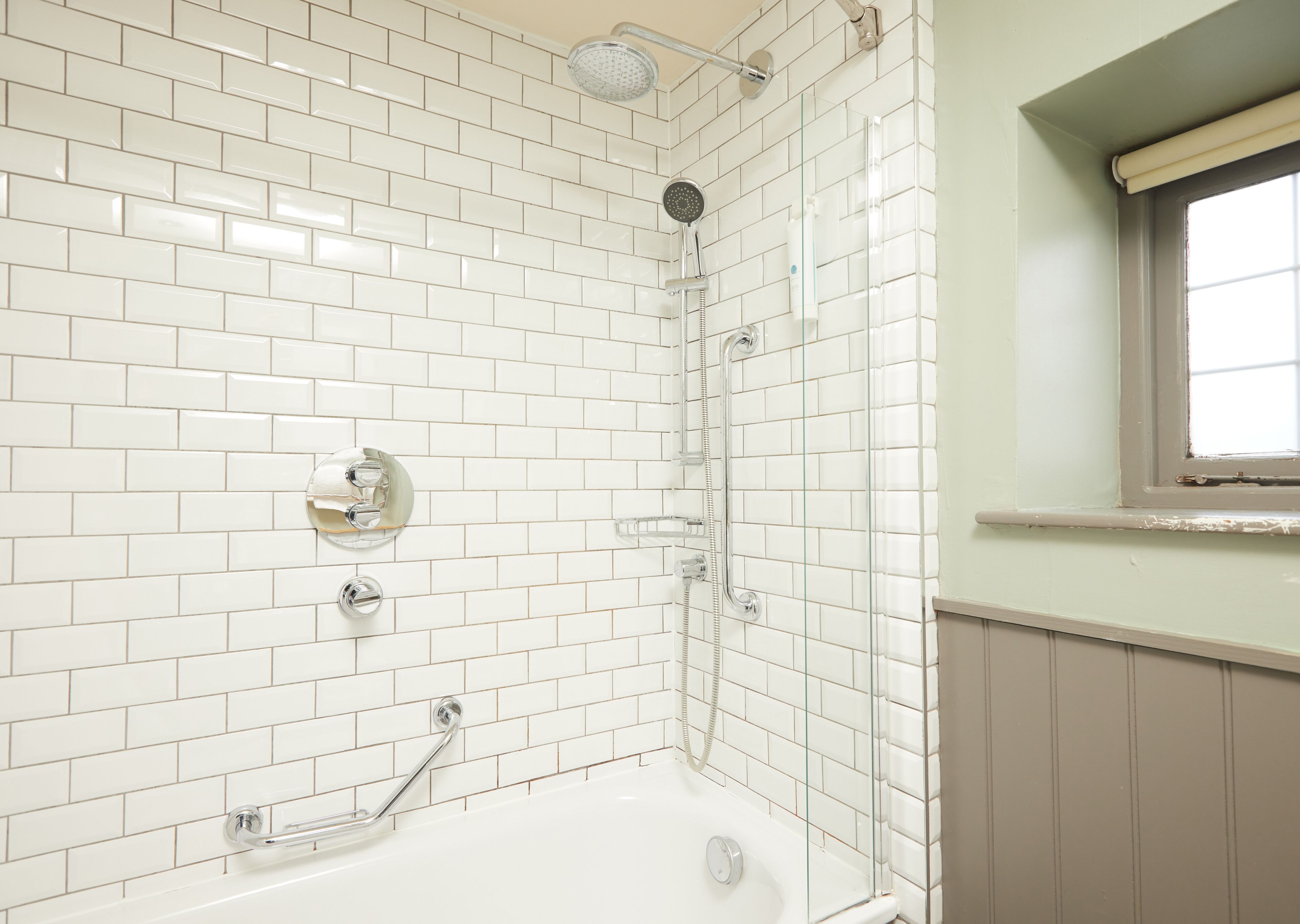 A bathroom with white subway tiles, a bathtub, a showerhead, and a window.