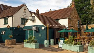 Een traditionele pub met een bord waarop 'The Red Lion' staat en een groen dak over de buitenplaats.
