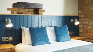 Cama bem arrumada com almofadas estampadas em azul, cabeceira de madeira e duas luminárias fixadas na parede.