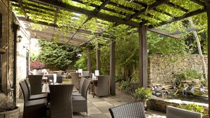 Un espace extérieur aménagé en terrasse, avec des meubles en osier, des murs en pierre et un petit élément décoratif aquatique.