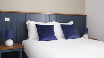 A neatly made bed with white and dark blue pillows, two bedside lamps, and a wooden headboard.