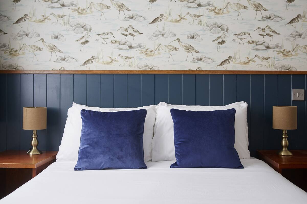 Ein Hotelzimmer mit einem Bett, zwei Nachttischen und Lampen. Die Wand ist mit Vogel-Tapete versehen.