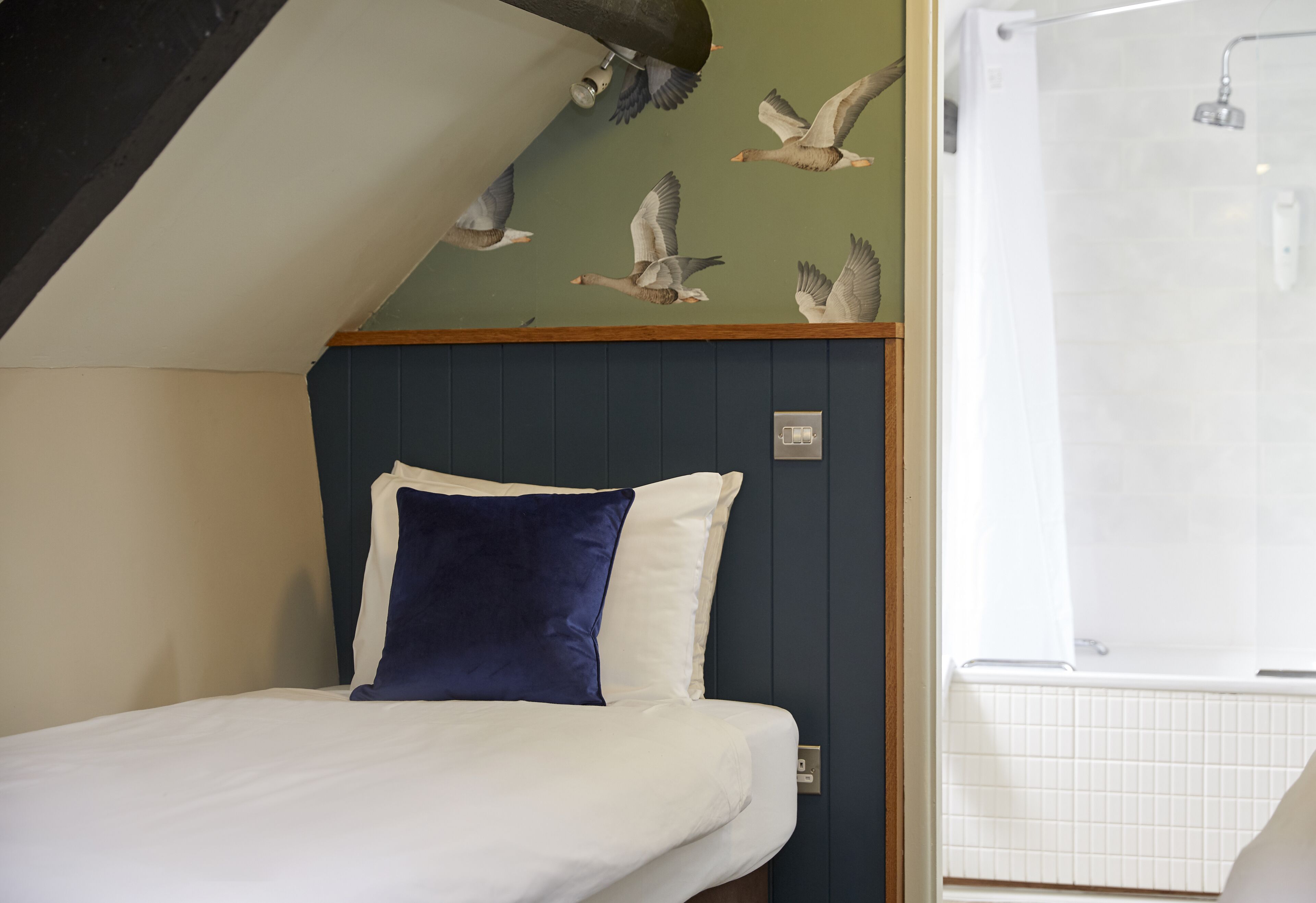 A bedroom with a bed, a blue pillow, and a wall mural of birds.