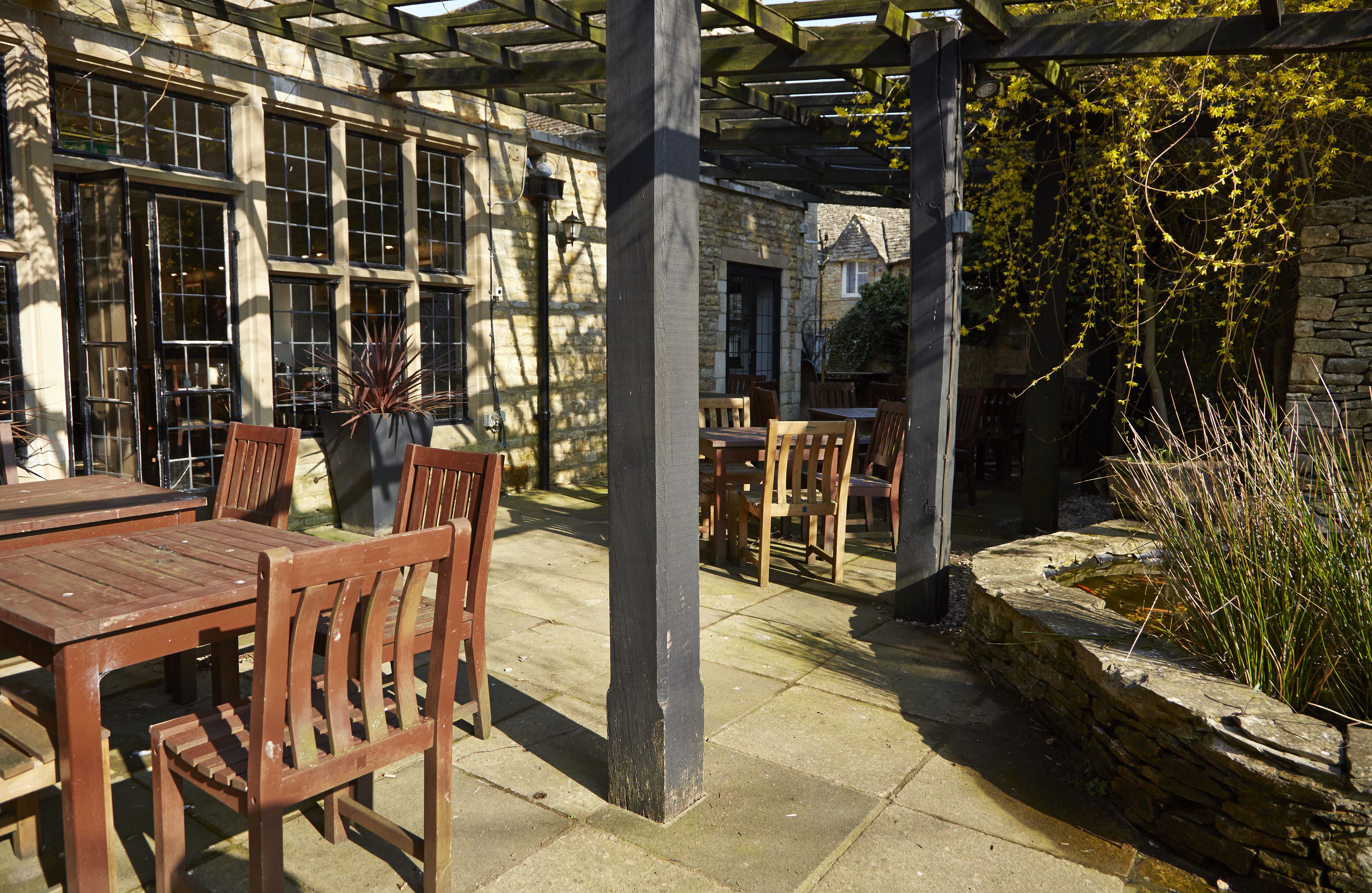 An outdoor patio area with stone walls, wooden tables and chairs, and a small water feature.
