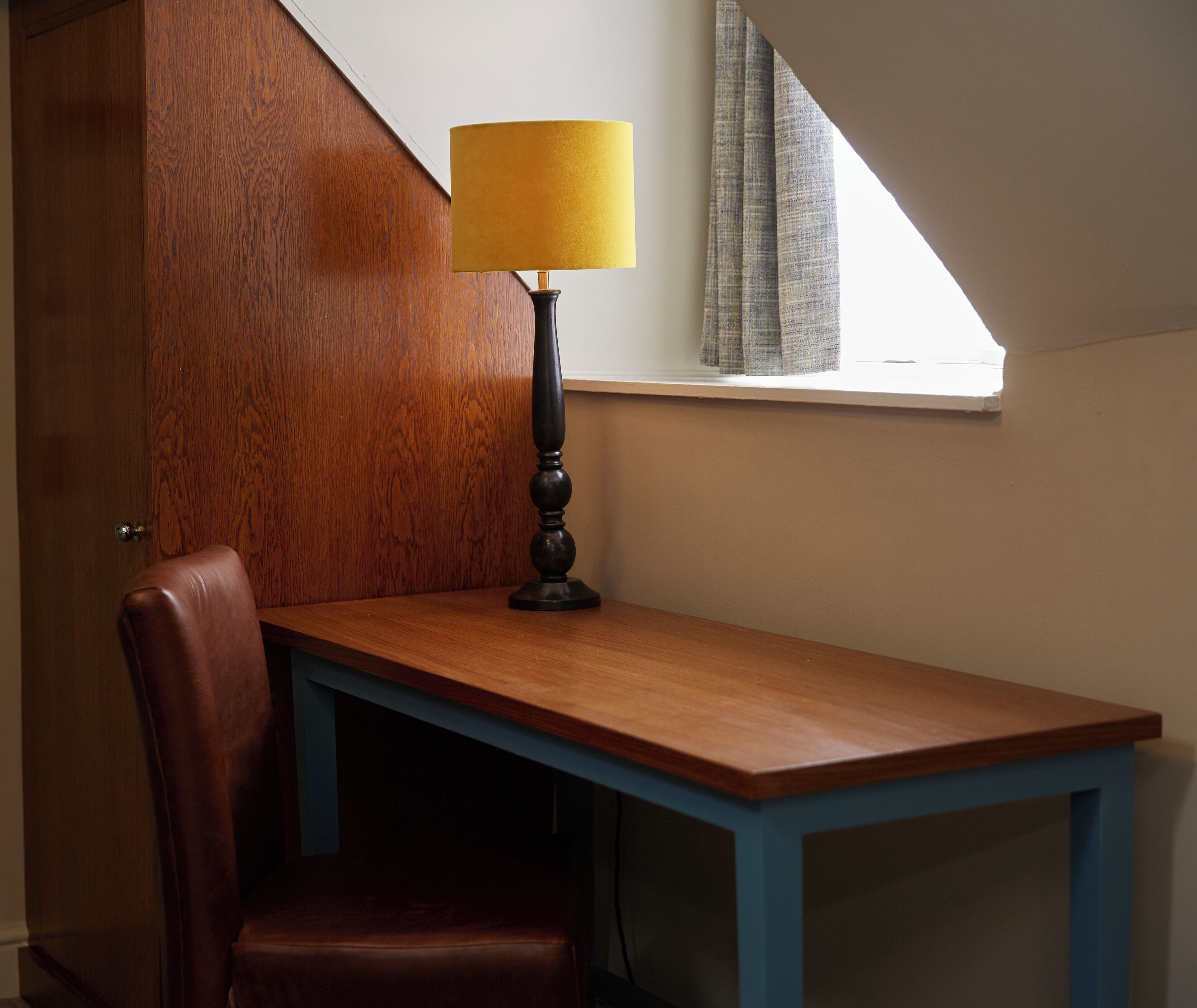 Un escritorio de madera con una lámpara, una silla y una ventana con cortinas.