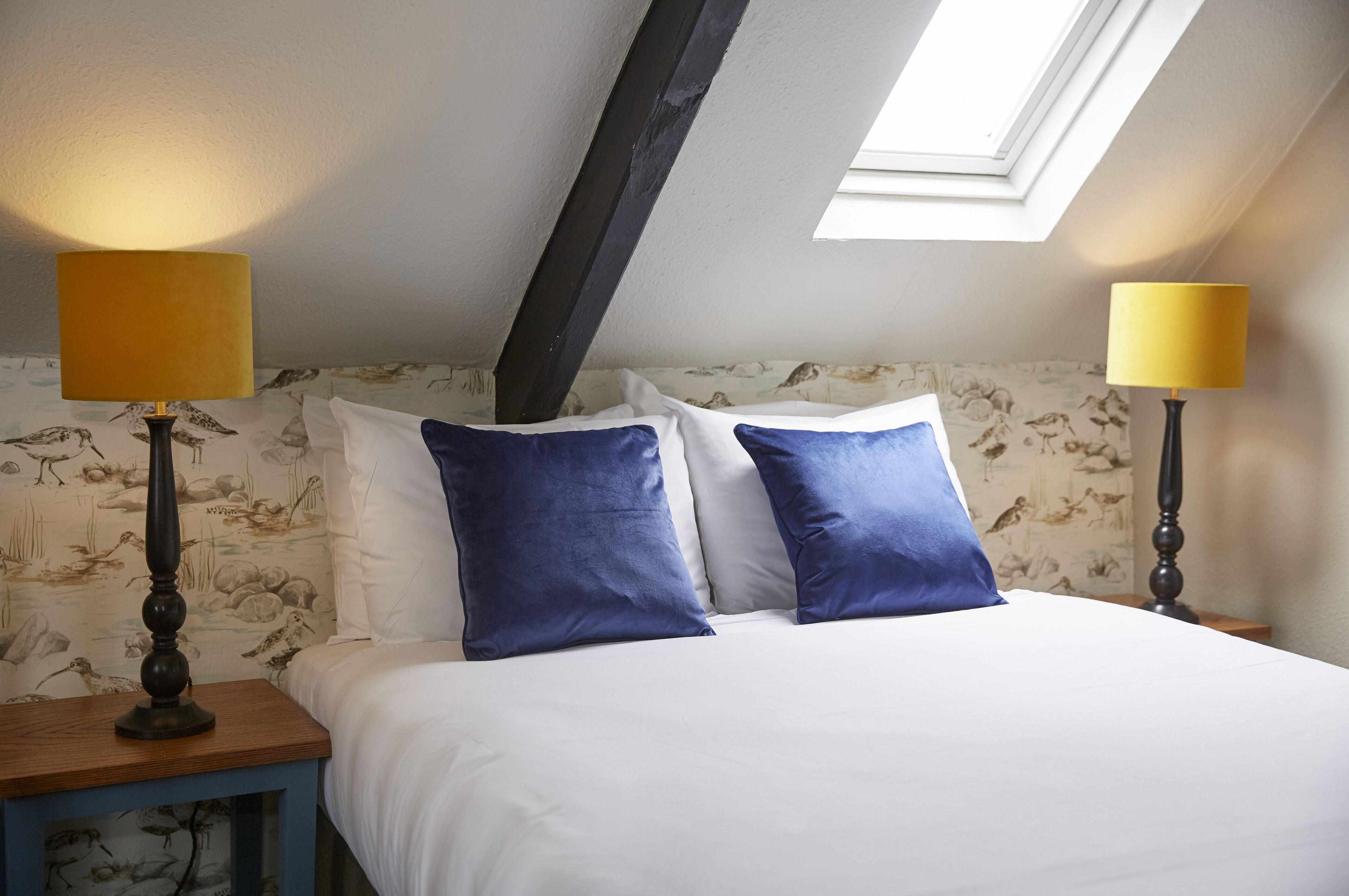 A bedroom with a skylight, two bedside lamps, and a floral wallpaper.