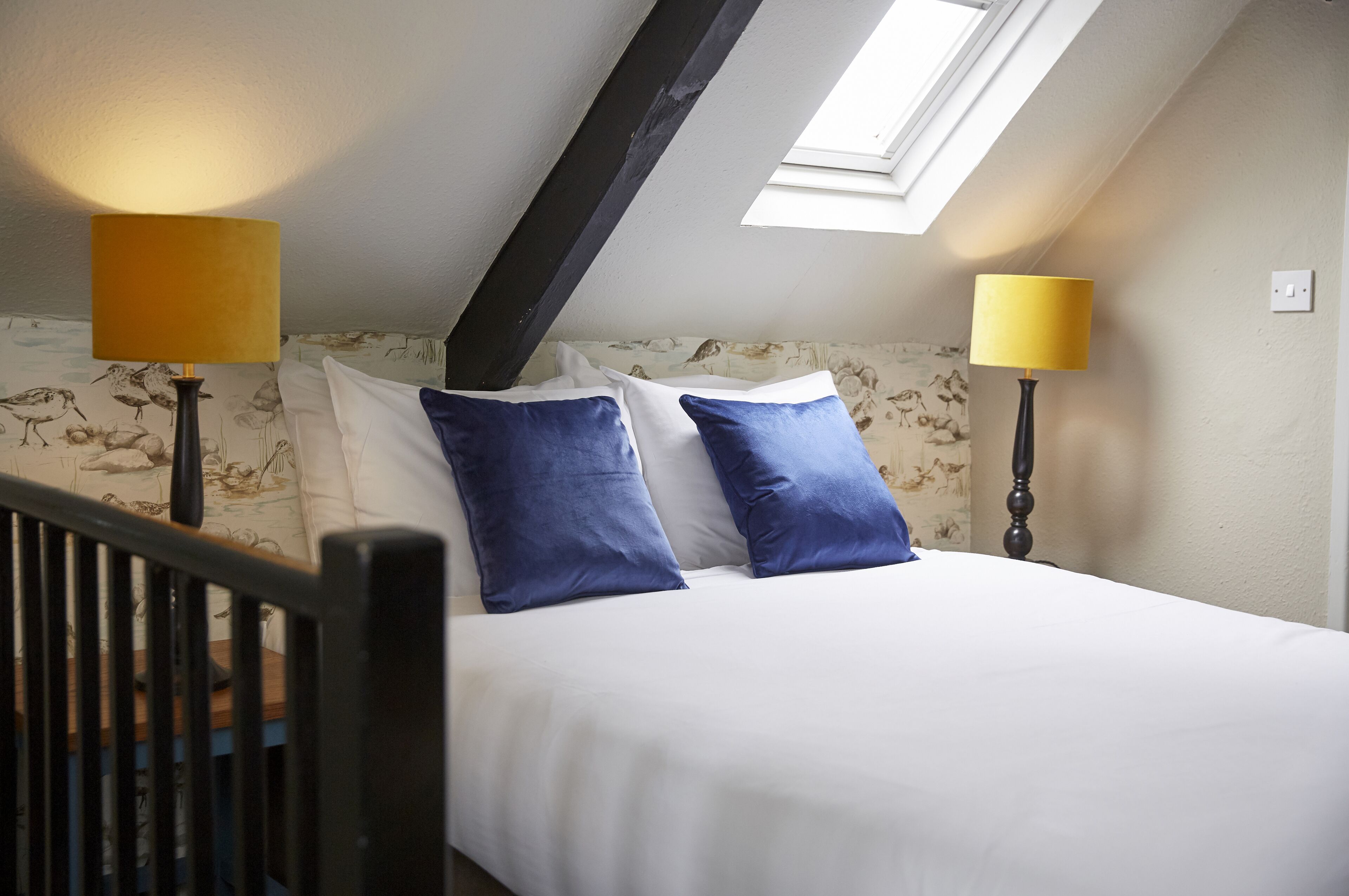 Een slaapkamer met een dakraam, twee bedlampen en een bed met wit- en blauw beddengoed.