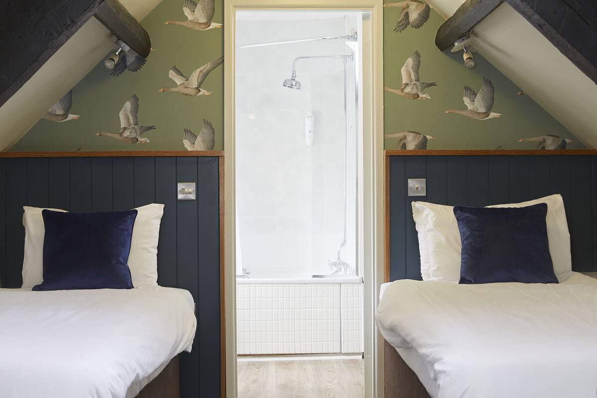 Ein Zimmer mit zwei Betten, einer Dusche und einer Vogel-bemalten Decke.