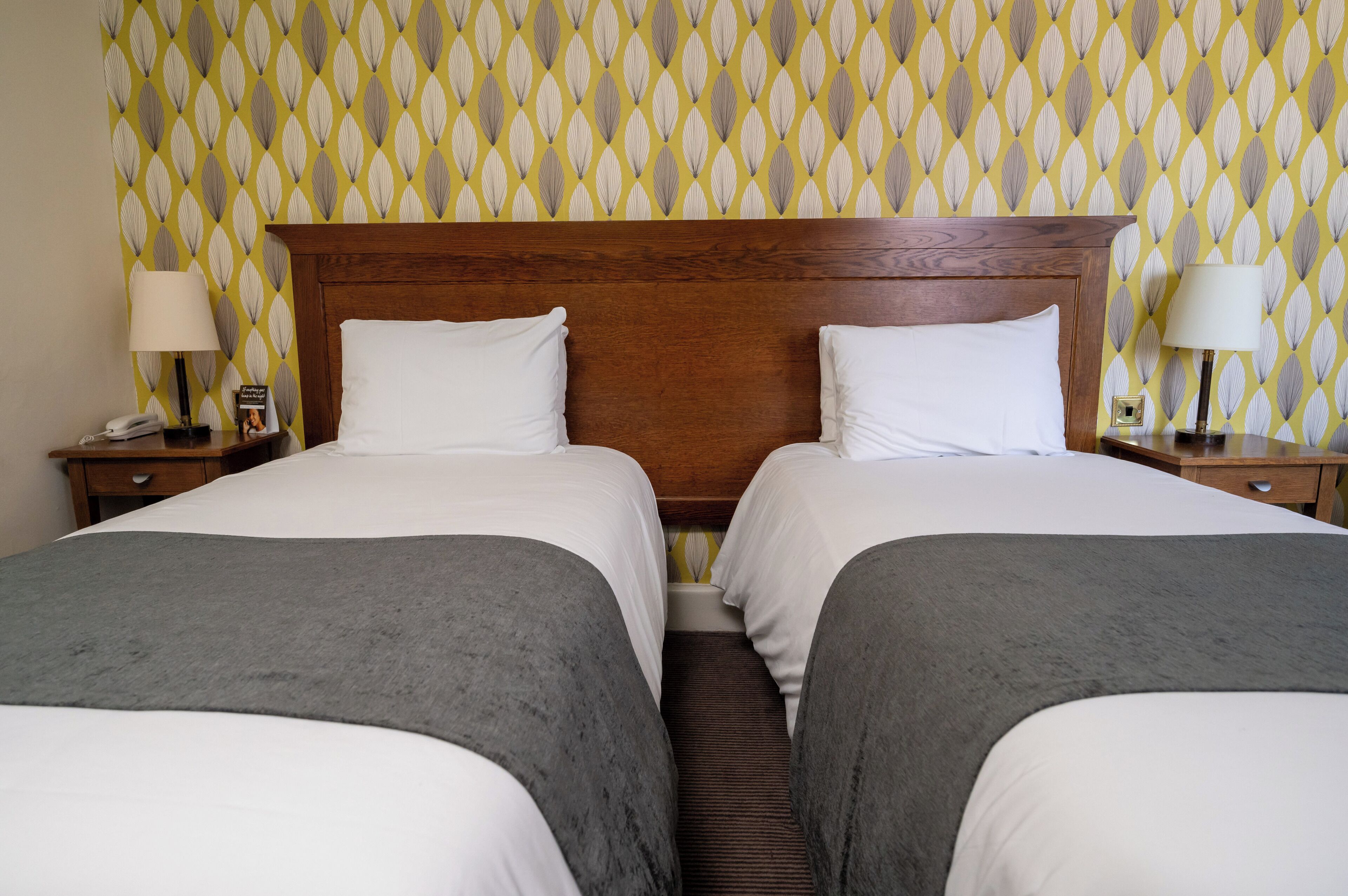 A hotel room with two beds, a wooden headboard, and patterned wallpaper.