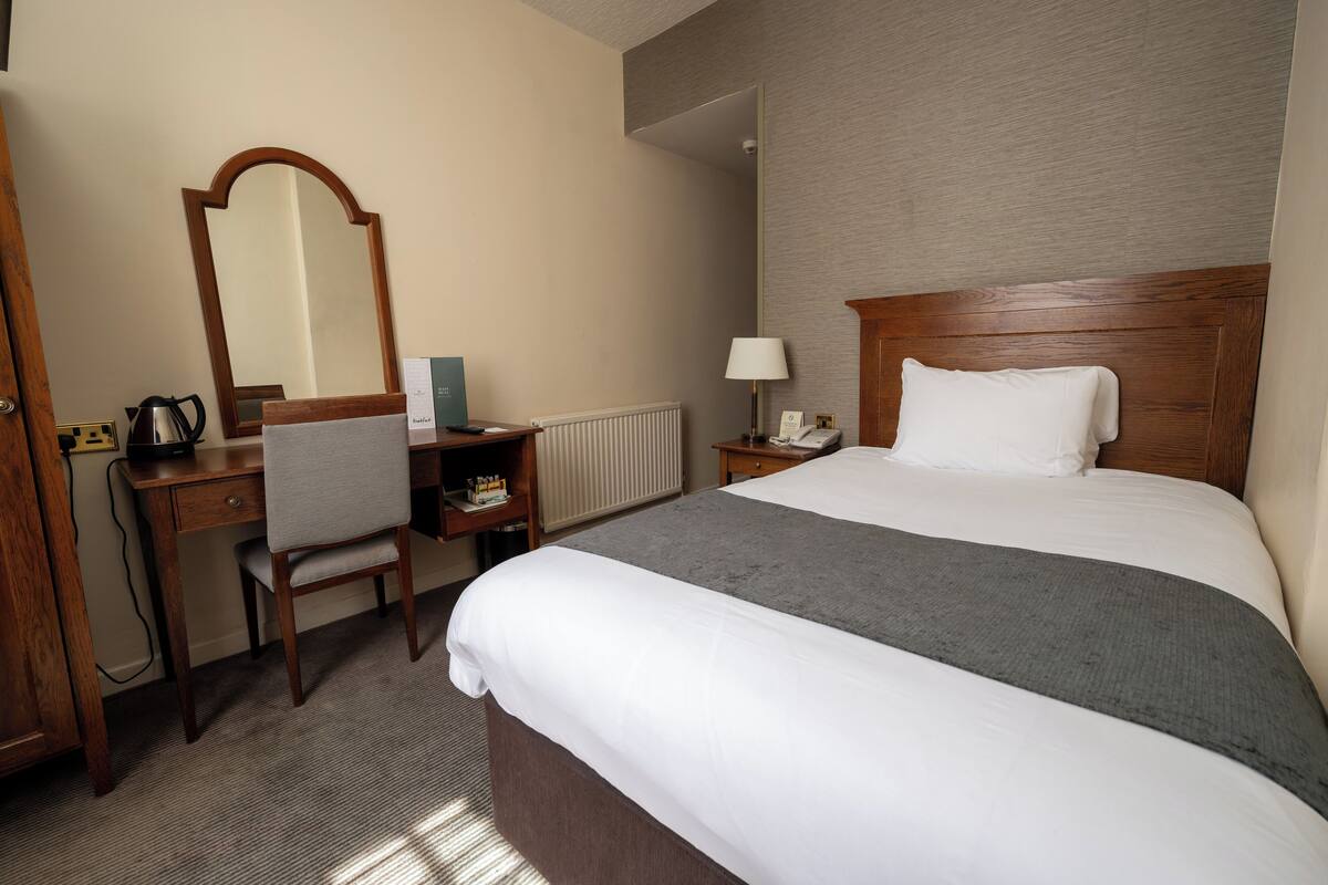 Ein Hotelzimmer mit Bett, Schreibtisch, Stuhl, Spiegel, Lampe und Telefon.