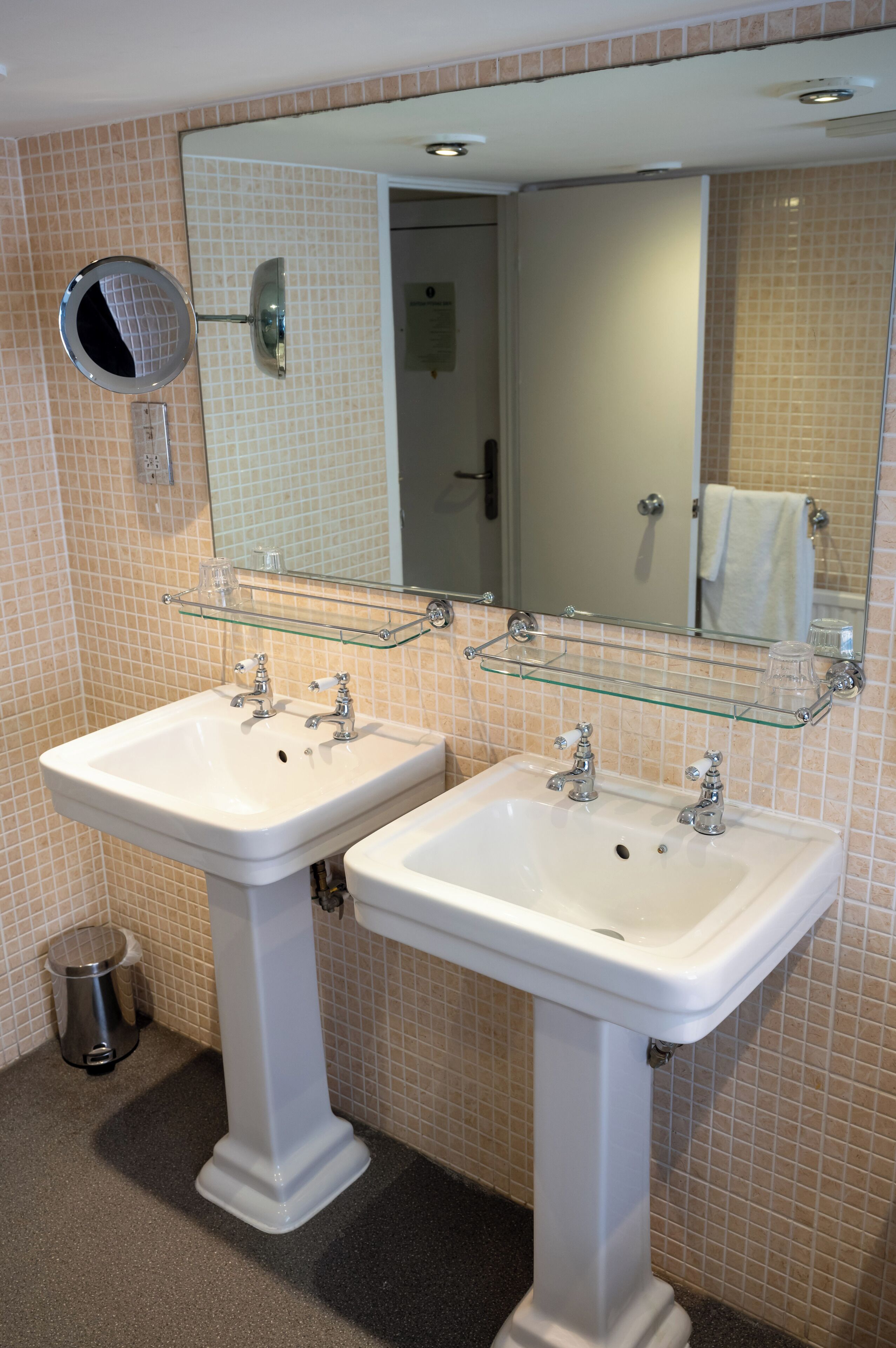 A bathroom with two white sinks, a glass shelf above them, and a mirror above the sink.