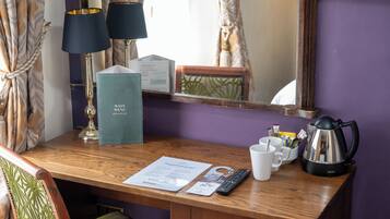 A wooden desk with a remote control, a menu, a kettle, and a cup.
