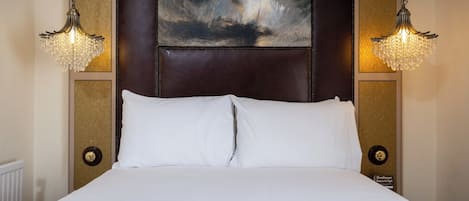 A hotel room with a large bed, two wall-mounted chandeliers, a dark headboard, and a framed artwork above the bed.