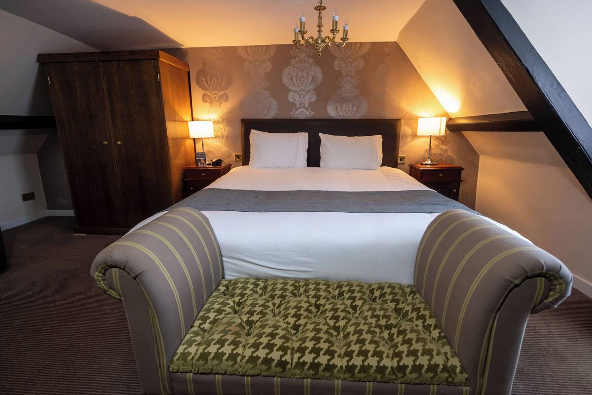 Ein Schlafzimmer mit einem großen Bett, zwei Nachttischlampen, einem Holzschrank und einem grünen Ohrensessel.