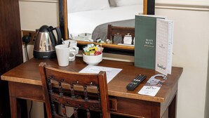 A hotel room with a wooden desk, a coffee maker, a bowl of snacks, a remote control, and a menu board. - Antelope Hotel by Greene King Inns (Poole)