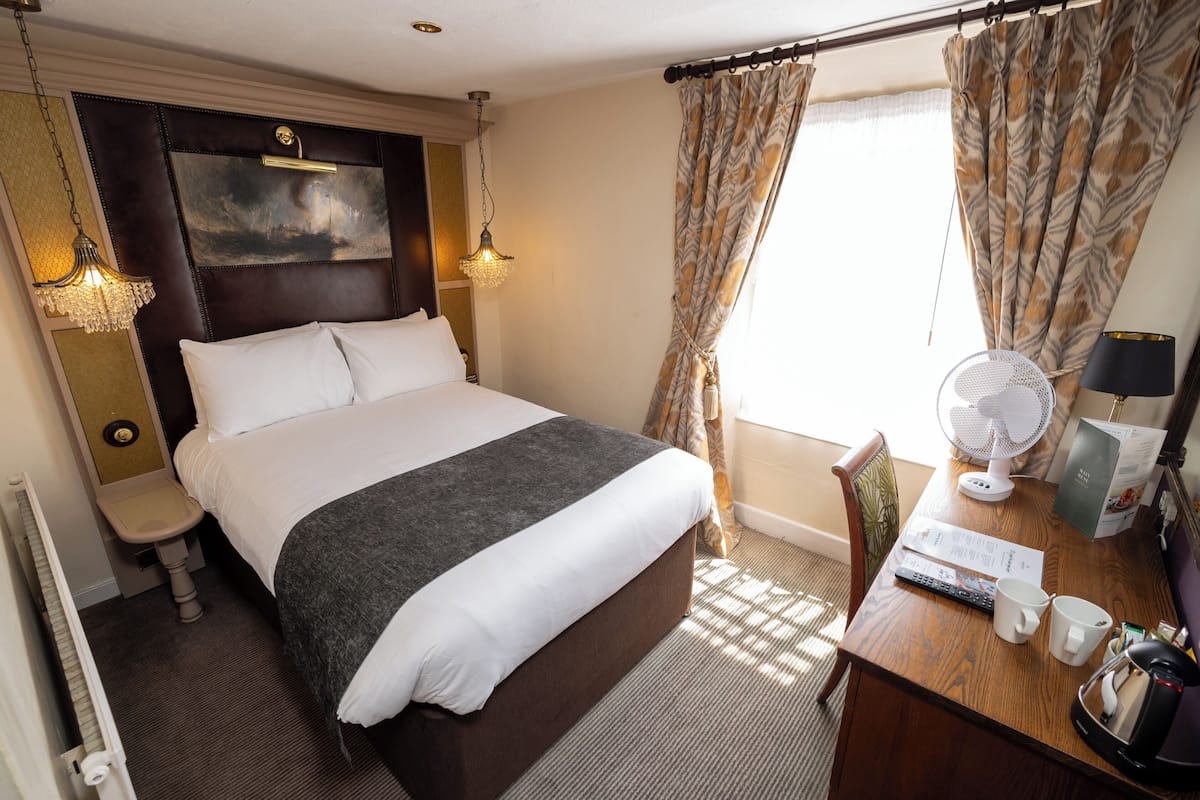 Ein Hotelzimmer mit einem großen Bett, Nachttischlampen, einem Schreibtisch mit Ventilator und einem Fenster mit Vorhängen.