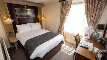 Habitación de hotel con una cama grande, lámparas de noche, un escritorio con ventilador y una ventana con cortinas.
