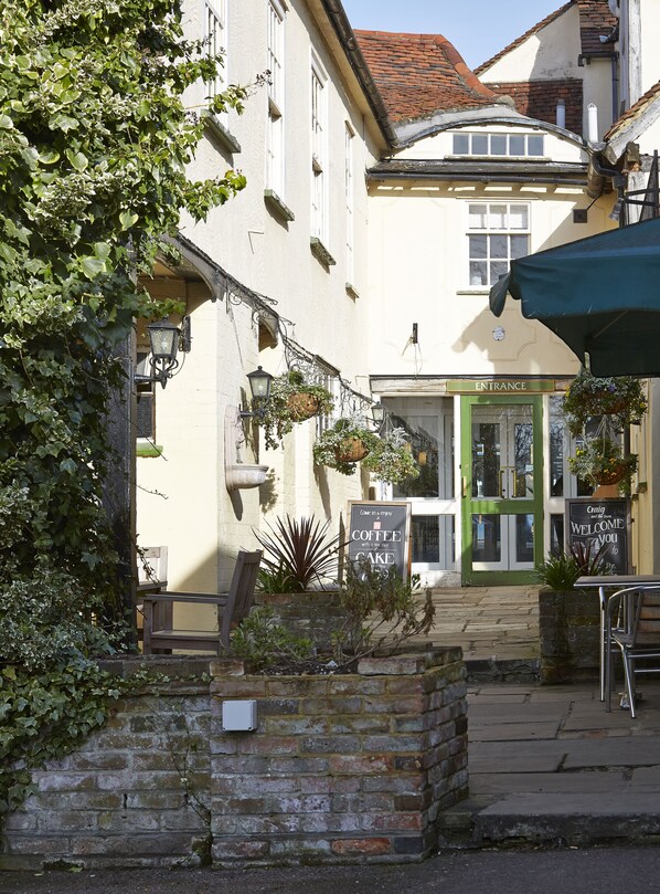 A quaint cafe with a green door, outdoor seating, and hanging plants.