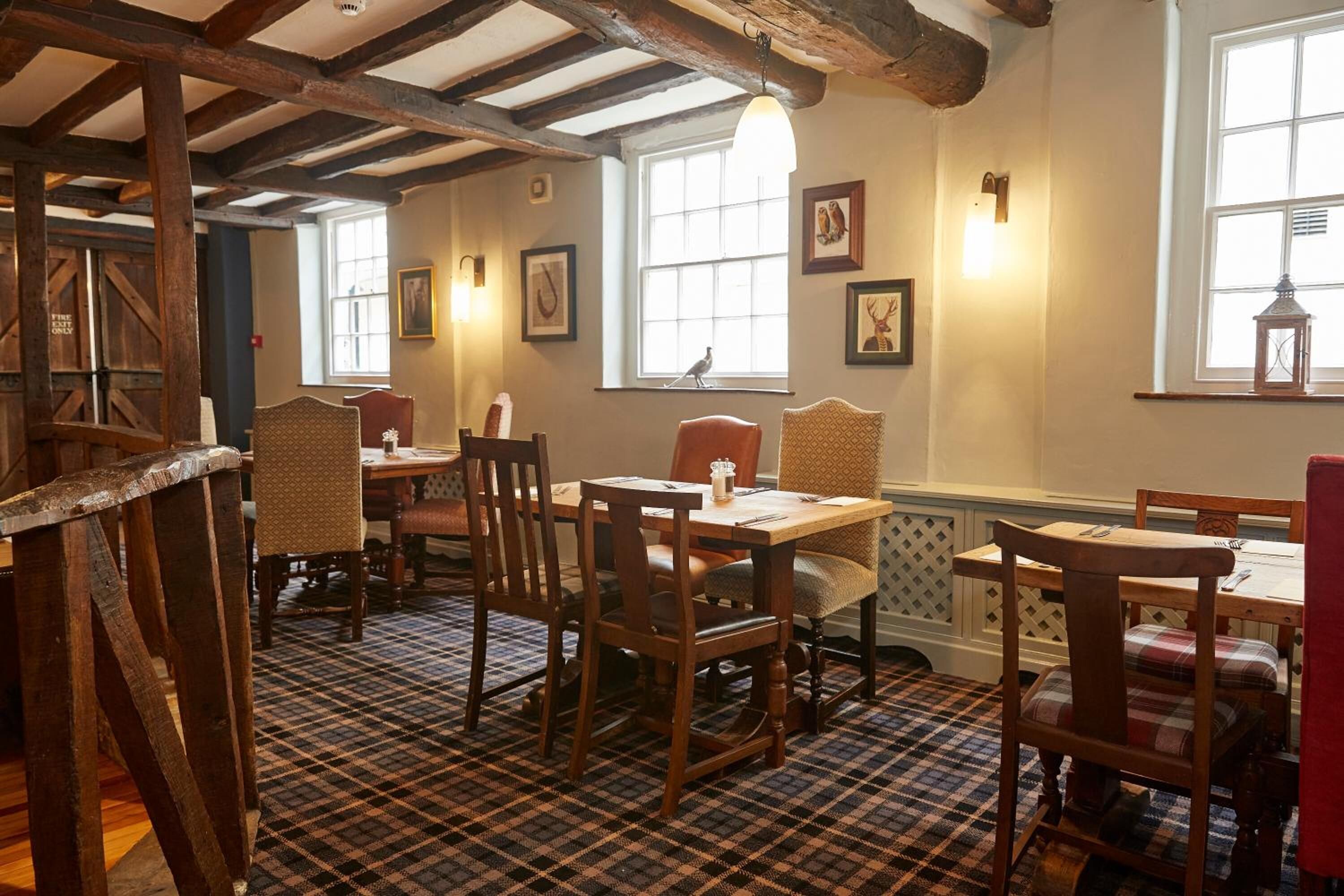 A dining area with wooden tables and chairs, a checkered floor, and framed pictures on the walls.