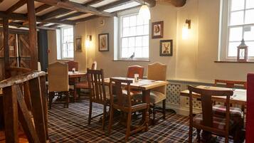 A dining area with wooden tables and chairs, a checkered floor, and framed pictures on the walls.