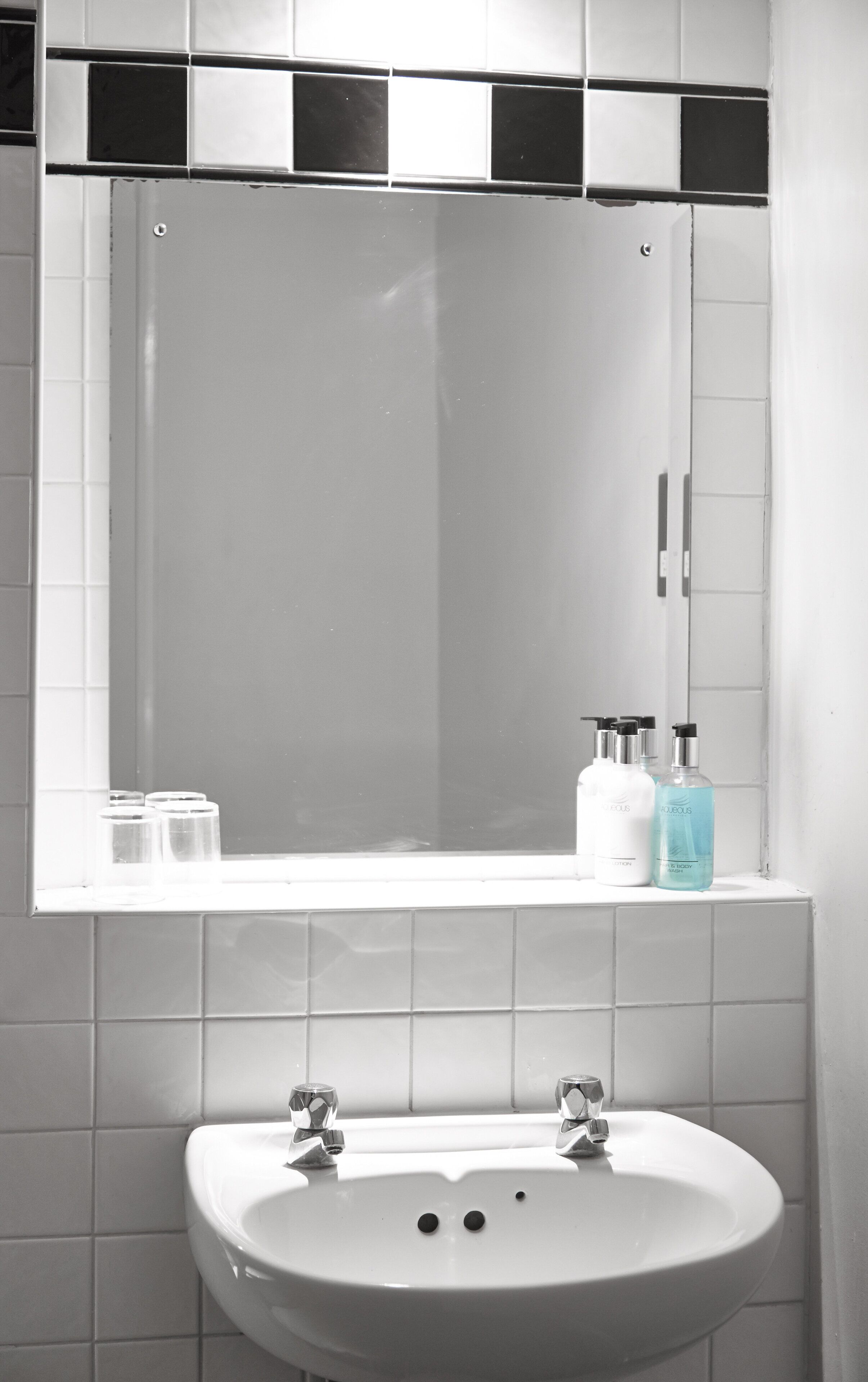Un baño con un lavamanos blanco, un espejo encima y dos botellas de jabón para manos sobre el borde del lavamanos.
