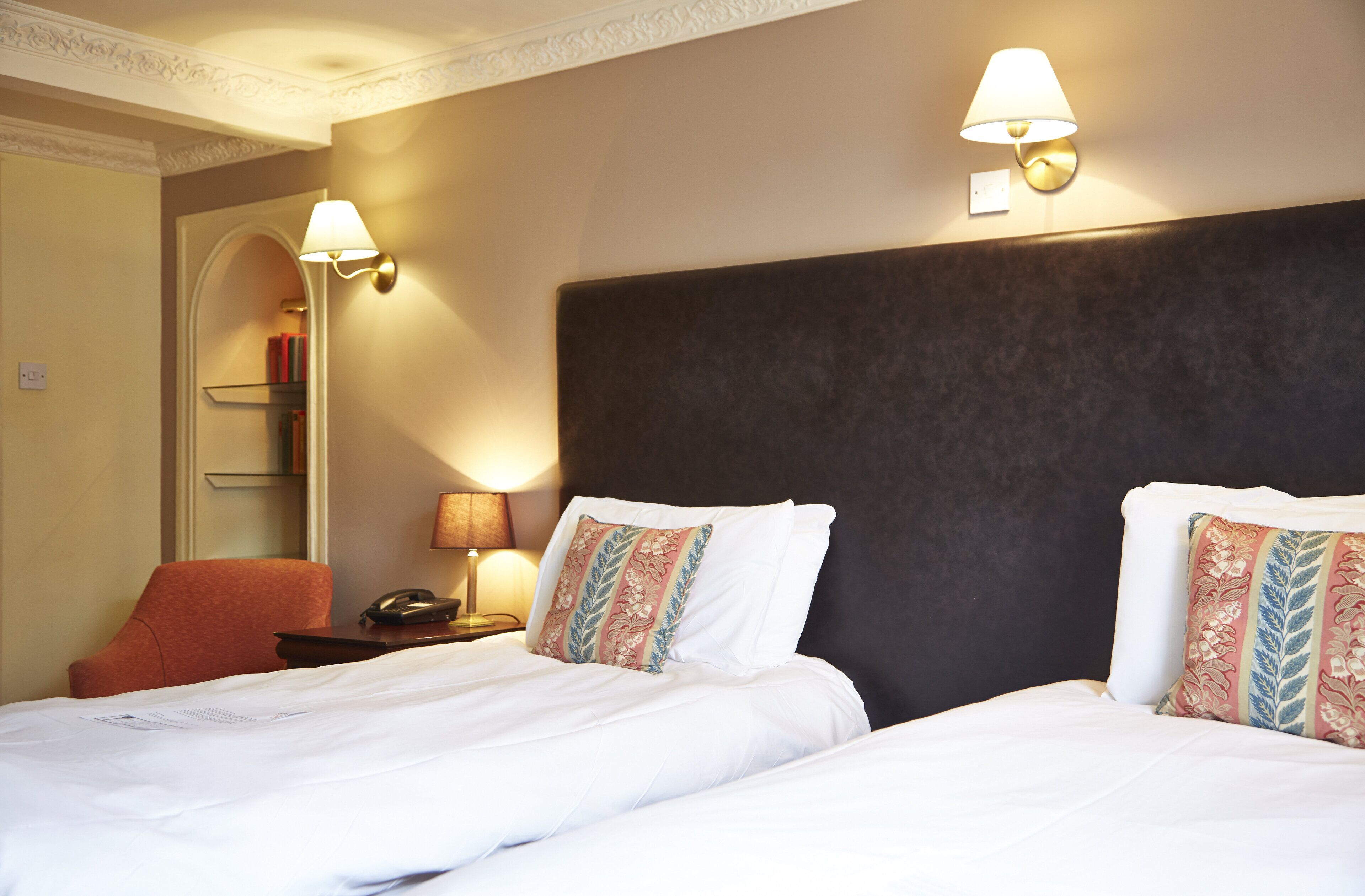 A hotel room with two beds, a nightstand, a lamp, and a chair.