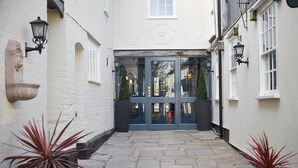 A narrow stone-paved courtyard with a double door entrance, flanked by white walls and black-framed windows. - White Hart Hotel by Greene King Inns (Colchester)
