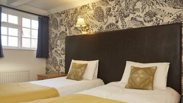 Una habitación de hotel con dos camas, una mesita de noche, una lámpara y una ventana con cortinas.