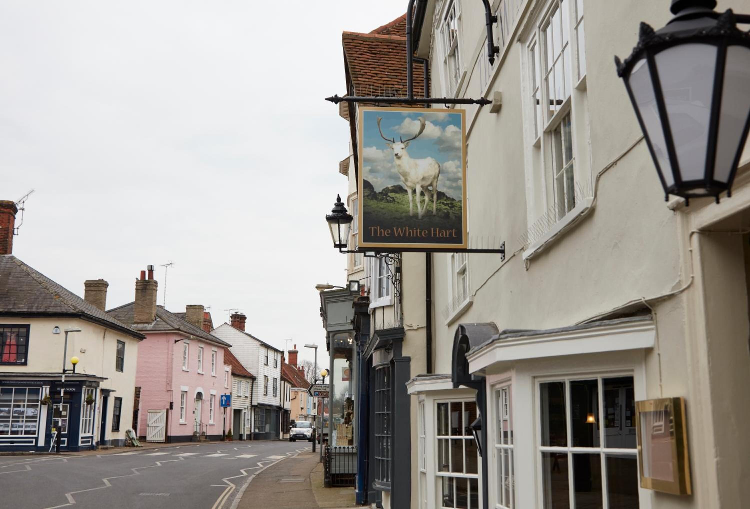 A street view with a pub named 'The White Hart' featuring a sign with a white stag.